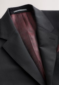 Veste de costume noire sur mesure avec doublure intérieure bordeaux à motifs et revers crantés, présentée à plat sur une surface claire.