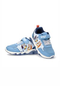 Zapatillas deportivas azules que combinan materiales lisos y texturizados, con una correa de velcro y un gráfico de perros animados en cada lado.