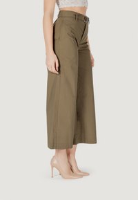 Pantaloni a gamba larga verde oliva con vita alta e cintura. Realizzati in tessuto morbido, presentano una piega sulla parte anteriore. Abbinati a tacchi alti nudi.