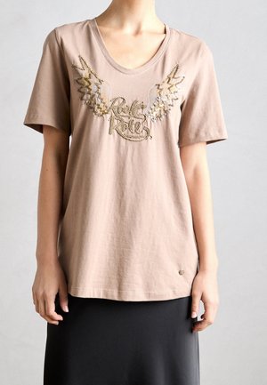 Beżowy t-shirt z krótkim rękawem z złotymi cekinowymi skrzydłami i haftem z napisem "Rock & Roll", noszony z czarną spódnicą.