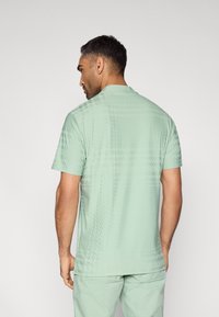 Πράσινο ανοιχτό πουκάμισο με κοντά μανίκια που διαθέτει διακριτικό γεωμετρικό σχέδιο, λεία υφή και άνετη εφαρμογή, με ίσια τελειώματα και γιακά.