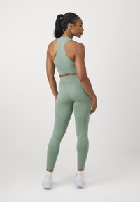 Ensemble de sport vert clair comprenant un crop top sans manches et un legging taille haute avec un motif texturé, associé à des baskets blanches.