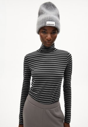 Schwarz- und grau gestreifter Rollkragenpullover, kombiniert mit einer grauen Strickmütze mit einem weißen Etikett. Die Mütze hat ein weiches, strukturiertes Aussehen.