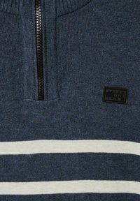 Gebreide rits-sweater in donkerblauw met witte horizontale strepen. Heeft een geribde kraag en een klein zwart logo-patch.