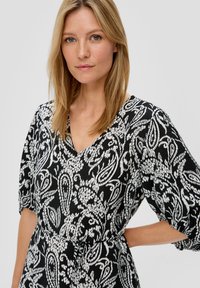 Musta-valkoinen kuviollinen mekko, jossa on V-pääntie, lyhyet puff-hihat ja kireä vyötärö. Rakenteellinen kangas, jossa on kukkakuvioita ja paisleyn muotoja.