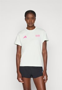 T-shirt in cotone verde chiaro con maniche corte, caratterizzata da un logo rosa per il BMW Berlin Marathon e tre strisce diagonali rosa a sinistra.