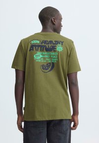 Olijfgroene katoenen T-shirt met korte mouwen, met opvallende tekstgrafieken in groen en zwart over gezond eten op de achterkant.