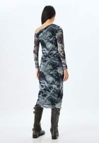 Lang, fitted jurk van doorschijnende stof met een abstracte print in blauw en grijs, voorzien van lange mouwen en een off-the-shoulder ontwerp. Zwarte kniehoge laarzen.