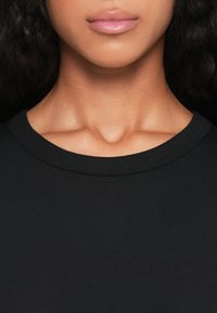Schwarzes Rundhals-T-Shirt, gerippter Halsausschnitt, glatte Textur, enganliegendes Design, das den natürlichen Hautton und das Schlüsselbein betont.