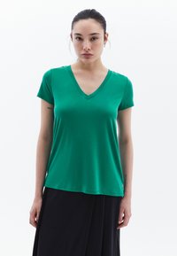 Camiseta verde de cuello en V hecha de tejido suave y liviano. Mangas cortas con un ajuste relajado, combinada con una falda negra fluida. Textura suave.
