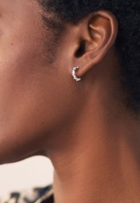 Silberner Creolen-Ohrring, verziert mit klaren rechteckigen und runden Edelsteinen, mit einem geschwungenen Design, das das Ohrläppchen umschmeichelt.