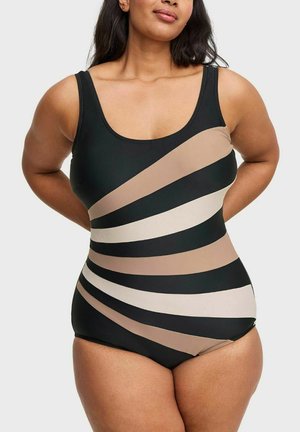 Vrouw in een zwart eendelig badpak met beige en tan diagonale strepen, staand met haar handen achter haar rug.