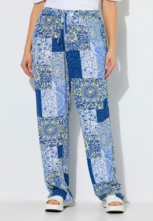 Rennot siniset tilkkupainokuvioiset housut, joissa on keltaisia ja valkoisia kukkakuvioita, yhdistettynä valkoisiin avokkailla varustettuihin korokesandaaleihin valkoisella taustalla.