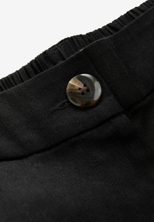 Cinturilla de tela negra con elástico fruncido, que presenta un botón redondo con un patrón y detalles de costura. Primer plano del material.