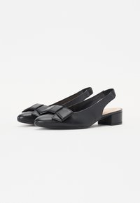 Sorte slingback-sko med rundt tå, med en stor sløyfe på vampen og en lav blokkhelt. Glatt skinntekstur.
