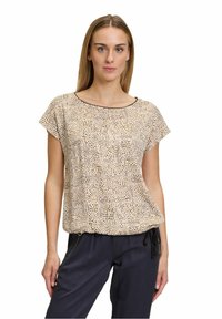 Krátký béžový top s texturovaným tečkovaným vzorem; kulatý výstřih, volný střih a kontrastní černé lemování. Kombinováno s tmavými kalhotami.