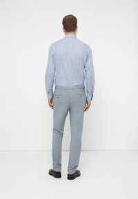 Hellblau karierter Hemd mit langen Ärmeln, kombiniert mit hellgrauen Hosen und dunklen Schuhen, von hinten vor einem weißen Hintergrund betrachtet.