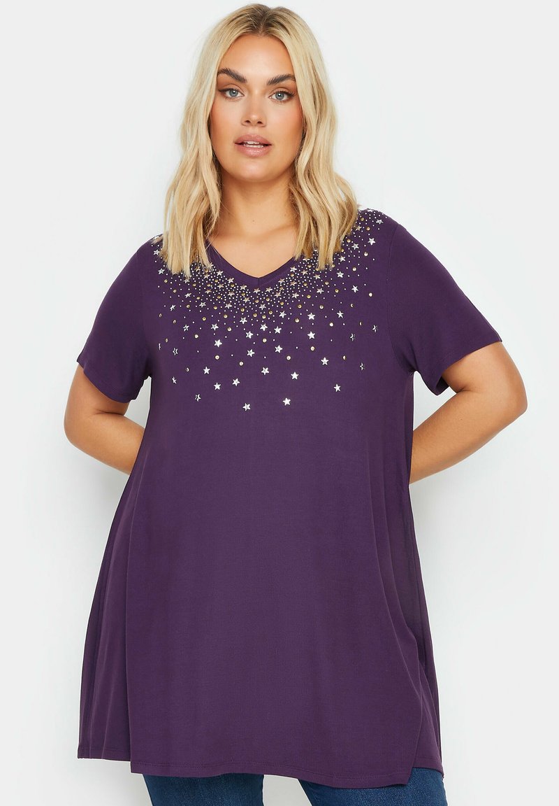 V-kauluksellinen violetti t-paita, lyhyet hihat ja tähkäkuvioinen helmikoristelu rinnassa. Pehmeä kangas ja rento istuvuus.