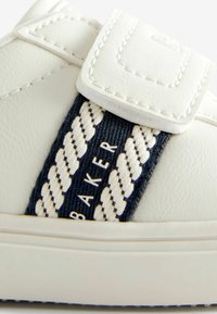 Valkoiset sneakersit, joissa on tarranauha, sisältävät tummansinisen kudotun nauhan, jossa on punottu rakenne ja "BAKER"-brändäys kultaisena. Sujuva nahkapinta.