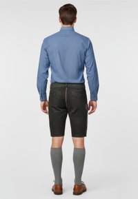 Blå långärmad skjorta i kombination med svarta shorts, med en texturerad design och gula sömmar, bärs med grå knä-length strumpor och bruna skor.