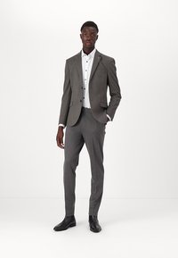 Férfi szürke öltöny, textúrált mintával, egygombos zakóval, fehér inggel és slim-fit nadrággal, fekete bokacsizmával párosítva.