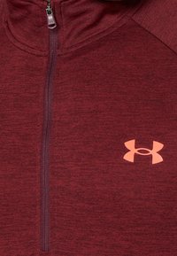 Mörkröd halvzip-pullover i mjukt tyg; har en texturerad yta och en kontrasterande rosa logga i nedre högra hörnet.