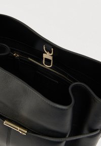 Εσωτερικό τσάντας από μαύρο δέρμα με χρυσά μεταλλικά μέρη, τσέπη με φερμουάρ και λεία υφή. Ανοιχτό πάνω μέρος χωρίς ορατά σχέδια ή διακοσμήσεις.