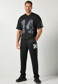 Czarny sportowy trykot z kamuflażową cyfrą "14", w zestawie z czarnymi spodniami z białą cyfrą "14" na nogawce i bocznymi paskami.