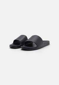 Schwarze Rutsch-Sandalen mit einer glatten, matten Oberfläche. Offenes Design mit breiten, geschwungenen Riemen. Leicht strukturierte Fußbett und Gummisohle.