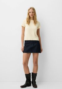 Lichtgele T-shirt met korte mouwen, gecombineerd met een donkerdenim rok en zwarte kniehoge laarzen met gespen. Minimalistisch ontwerp en fitted vorm.