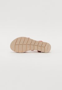 Sandale rouge avec une sangle ajustable, dotée d'un semelletté en caoutchouc texturé et d'une semelle intérieure beige et flexible avec un motif de crampons pour une meilleure adhérence.