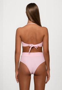 Twee-delig bikini set in lichtroze. Top met wikkeldesign en strik op de rug; hooggeknoopte broekjes met een zachte textuur en minimale bedekking.