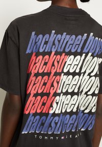 Black cotton t-shirt featuring "backstreet boys" text in red, white, and blue gradient, with a relaxed fit and crew neck design.