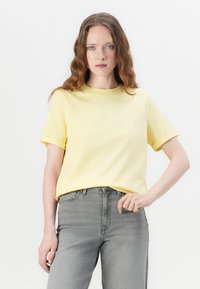 T-shirt jaune à manches courtes avec un col rond, en tissu doux, associé à un jean gris taille haute. Design simple, sans motifs visibles.