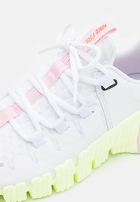 Vit sportskor med en strukturerad nätöverdel, rosa detaljer och en kraftig neongrön sula. Har vita snören och varumärkesdetaljer.