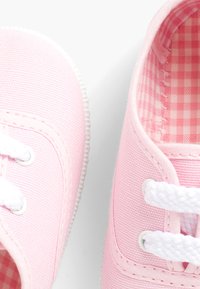 Scarpe da ginnastica rosa in tela con lacci bianchi, punta tonda, parte superiore texturizzata e foderatura a quadretti visibile all'interno.