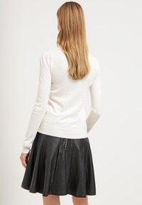 Pull léger crème à manches longues, associé à une jupe plissée en cuir noir avec un détail de fermeture éclair au dos.