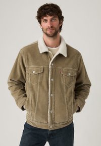 Veste en velours côtelé verte olive avec un col en sherpa blanc, comportant deux poches poitrine, des boutons en métal et une coupe décontractée.