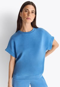 Niebieski, oversize bluza z krótkimi, podwiniętymi rękawami, gładką fakturą i okrągłym dekoltem. W komplecie z pasującymi dołem.
