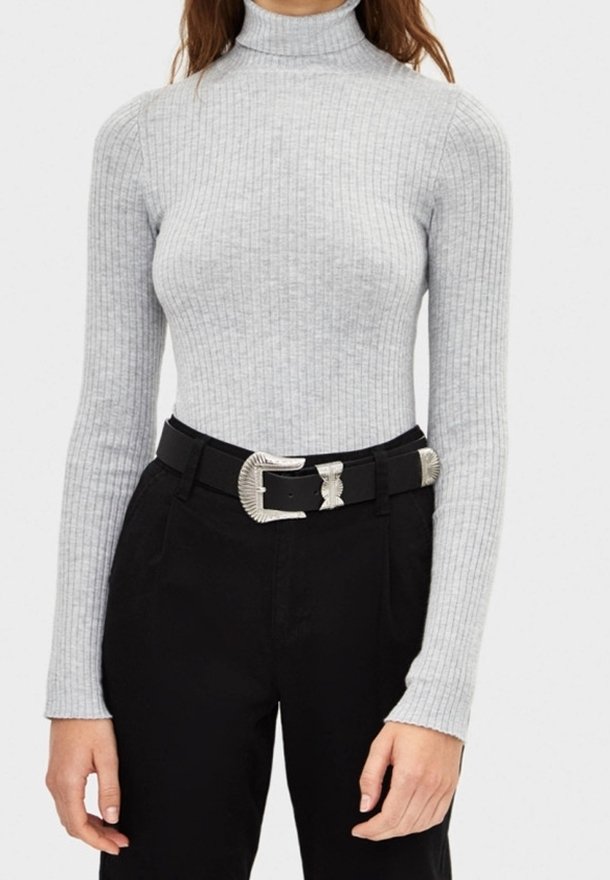 Haut à col roulé gris côtelé associé à un pantalon noir taille haute, avec une ceinture métallique dotée d'une boucle à motif unique.