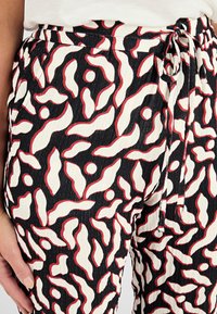 Pantaloni con vita elastica caratterizzati da un tessuto testurizzato con un audace motivo astratto nei toni del nero, bianco e rosso. Include un dettaglio con lacci regolabili.