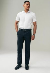 Weißes kurzärmeliges Hemd mit Knopfleiste, marineblaue Anzughose, schwarzer Gürtel und schwarze Schnürschuhe. Einfaches, maßgeschneidertes Design mit glatter Textur.