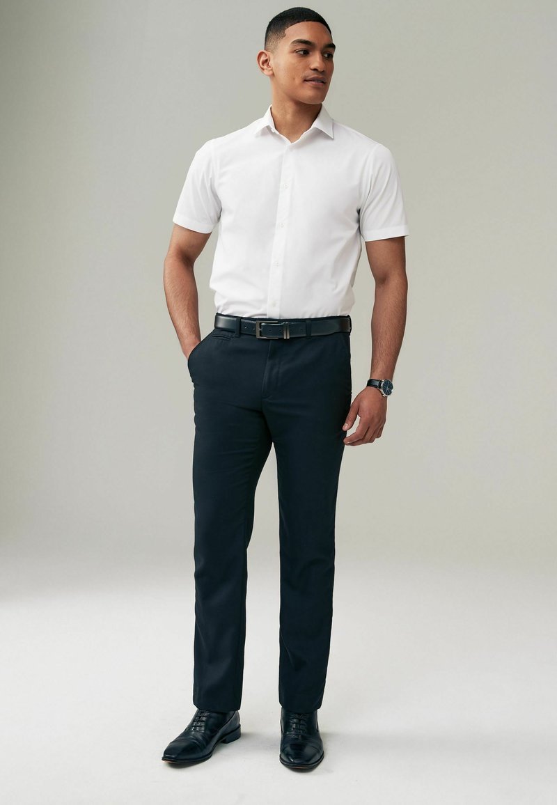 Weißes kurzärmeliges Hemd mit Knopfleiste, marineblaue Anzughose, schwarzer Gürtel und schwarze Schnürschuhe. Einfaches, maßgeschneidertes Design mit glatter Textur.