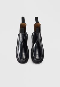Cizme de gleznă din piele neagră cu finisaj neted, panouri laterale elastice și cusături decorative. Au vârf rotund și cârlige pentru a fi trase.