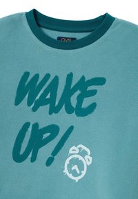 Sudadera de felpa turquesa con cuello redondo y un texto llamativo "¡DESPIERTA!" acompañado de un gráfico de un reloj de alarma blanco. Textura suave y diseño casual.