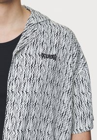 Korte mouwen shirt met een golvend zwart-wit patroon, kraag en geborduurd "PESCADOR" logo op de borst. Zachte stofstructuur.
