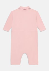 Mono rosa de manga larga con cuello tipo polo. Fabricado en un tejido suave, tiene una textura lisa y un ajuste relajado con piernas cortas.