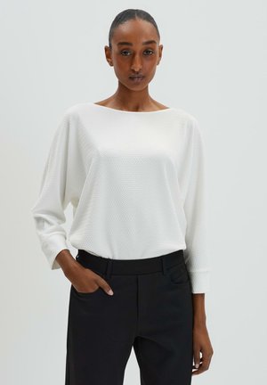 White textured long-sleeve top with a wide neckline, worn with high-waisted black trousers, featuring side pockets and a slim fit.