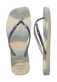 Pelēkas flip-flop sandales ar teksturētu pēdas zolīti un metāliskas sudrabotas spīdīgas siksniņas. Zolei ir smalka gradienta raksts ar logotipa detaļām.