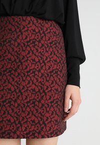 Sukně s leopardím vzorem v červené a černé barvě, s fitted střihem, texturovaným materiálem a pasem. V kombinaci s černým topem s nabíranými rukávy.